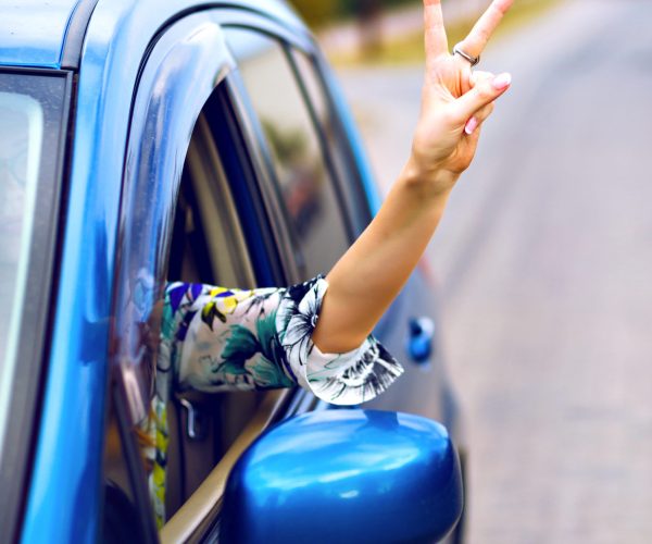 Young woman driving car at countryside , put her hand out of the car enjoy her freedom , making good yo science by her hand, travel vacation concept.